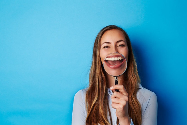 Brunette woman smiles as she holds a magnifying glass up to her teeth