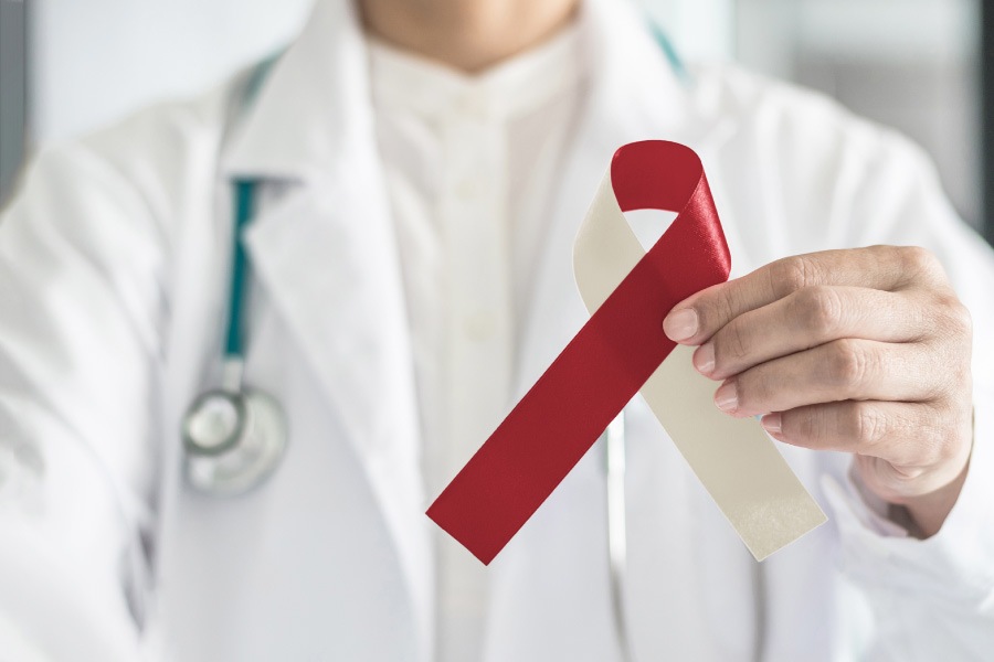 Dentist with a stethoscope holds up a burgundy and ivory ribbon for oral cancer awareness