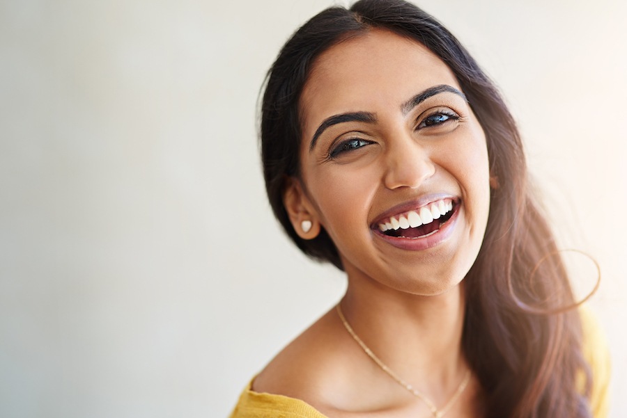 Brunette brown woman with dental veneers smiles broadly