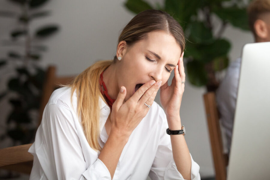 Brunette woman yawns at work during the day because she has sleep apnea and isn't sleeping well